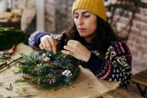 Portrait of woman squatting at table and making Christmas wreath — Stock Photo