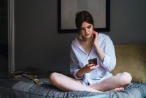 Portrait of woman sitting in bed and browsing smartphone — Stock Photo
