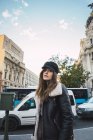 Брюнетка дівчина в теплій пальто і cap ходьба по вулиці і дивлячись на камеру — стокове фото