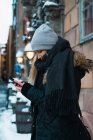 Vista lateral de mujer rubia con teléfono inteligente en la calle de invierno - foto de stock