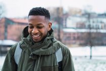 Portrait of smiling man wearing green coat and backpack looking down — Stock Photo