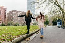 Ruiva menina ajudando namorada equilibrar enquanto caminha sobre afiação — Fotografia de Stock