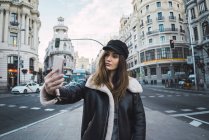 Bruna donna in cap prendere selfie sulla scena di strada — Foto stock