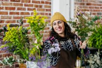 Retrato de mujer sonriente mirando la flor en la mano en el atelier floral - foto de stock
