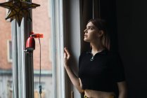 Side view of young woman posing by window at home dramatically looking up. — Stock Photo