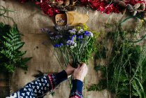 Растениеводческие женские руки, составляющие цветочный букет поверх мешочка на столе — стоковое фото