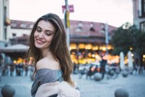 Side view of smiling brunette woman posing on urban street. — Stock Photo