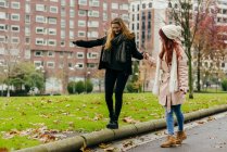 Pretty woman walking with friend and helping her to balance on edging — Stock Photo