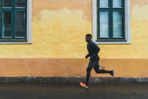 Seitenansicht eines Mannes in warmer Sportbekleidung beim Joggen entlang der Hausfassade — Stockfoto