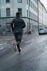 Вид сзади на бегуна в теплой спортивной одежде, бегущего по улице — стоковое фото