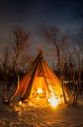 Tent with bonfire inside at frosted forest covered with snow at night. — Stock Photo