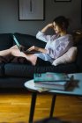 Вид збоку жінки, що сидить з ноутбуком на дивані — стокове фото