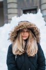 Портрет блондинки в капюшоне, позирующей в зимнем городе и смотрящей в сторону — стоковое фото
