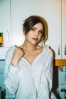 Portrait of woman sensually posing in shirt at kitchen and looking at camera — Stock Photo