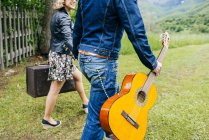 Crop couple holding hands and walking with guitar on green lawn. — Stock Photo