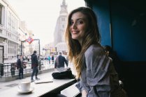 Досить молода жінка сидить вікна в кафе і дивлячись на камеру — стокове фото