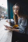 Retrato de menina morena bebendo café no café e navegando smartphone — Fotografia de Stock