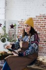Portrait of smiling woman in sweater and apron sitting with tablet in floral atelier and looking at camera — Stock Photo