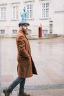 Side view of bearded man wearing coat and cap posing at street scene — Stock Photo