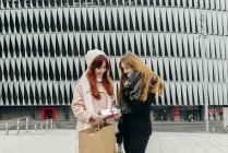 Front view of redhead girl giving gift to girlfriend at street scene — Stock Photo