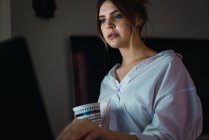 Portrait of woman in white shirt holding cup and using laptop — Stock Photo