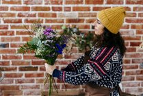 Side view of florist composing bouquet on background of loft brick wall — Stock Photo