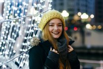 Sorrindo jovem mulher olhando para a câmera e posando na iluminação na rua . — Fotografia de Stock