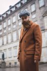 Ritratto di uomo barbuto in cappotto in posa per strada e guardando in basso — Foto stock