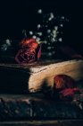Закрыть вид на высохшие розы и маленькие белые цветы на старой книге за сельским деревянным столом — стоковое фото