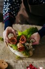Crop mains féminines en pull tricoté faisant composition florale sur la table — Photo de stock