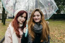 Portrait of two girls posing with umbrella in park and looking at camera — Stock Photo