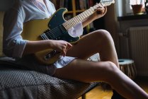 Кроп женщина сидит в тренере и играет на гитаре — стоковое фото