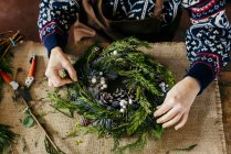 Руки цветоводов делают рождественский венок на мешочке за столом — стоковое фото
