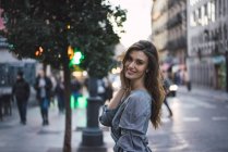Vue latérale de la femme brune souriante sur la rue urbaine — Photo de stock