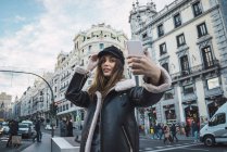 Vista de ángulo alto de la mujer morena en la tapa de tomar selfie en el teléfono inteligente en la escena de la calle - foto de stock