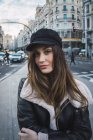 Portrait of brunette woman in stylish cap looking at camera on street — Stock Photo