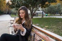 Retrato de mulher com smartphone no banco do parque — Fotografia de Stock