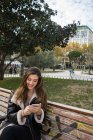 Ritratto di donna bruna sorridente con smartphone sulla panchina del parco — Foto stock