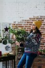 Side view of woman in knitted sweater and hat composing bouquet at flower shop — Stock Photo