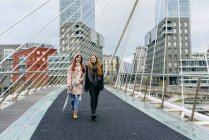 Vue de face de deux copines marchant sur un pont urbain — Photo de stock
