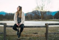 Портрет молодої дівчини, що сидить на сільському паркані в сільській місцевості і дивиться в сторону — стокове фото