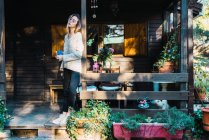 Jeune femme sensuelle prenant le café du matin dans une tasse tout en posant sur le porche de la maison en bois . — Photo de stock