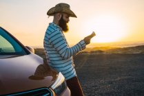 Side view of confident traveler leaning on car and reading map at shoreline — Stock Photo