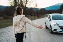 Visão traseira da menina gestos enquanto carona na estrada remota — Fotografia de Stock