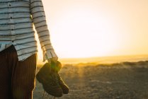 Crop macho carregando botas na mão e caminhando no vale de areia iluminada pelo sol — Fotografia de Stock