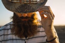 Бородатий чоловік ховає очі капелюхом на сонячне світло — стокове фото