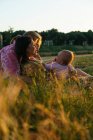 Vue latérale de la famille lesbienne heureuse avec enfant couché sur la pelouse au coucher du soleil — Photo de stock