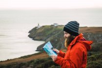 Vista lateral del hombre barbudo posando con mapa sobre colinas costeras - foto de stock