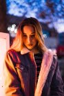 Junges blondes Mädchen posiert draußen im Lampenlicht und schaut in die Kamera — Stockfoto