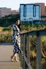 Side view of woman in beautiful dress posing on bridge with eyes closed at city park — Stock Photo